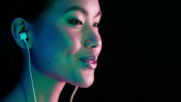 Приваблива молода азіатка освітлена неоновими вогнями Прослуховування музики в навушниках — стокове відео