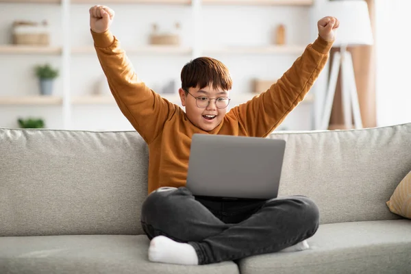 Happy teenager looking at computer screen and raising hands up — Zdjęcie stockowe