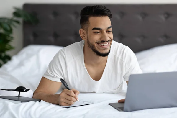 Online Education Concept. Arab Man Studying With Laptop While Lying In Bed — Stockfoto