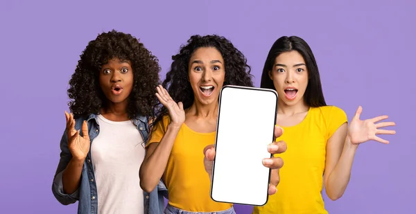 Εκπληκτικές πολυεθνικές κυρίες που δείχνουν smartphone με λευκή οθόνη — Φωτογραφία Αρχείου