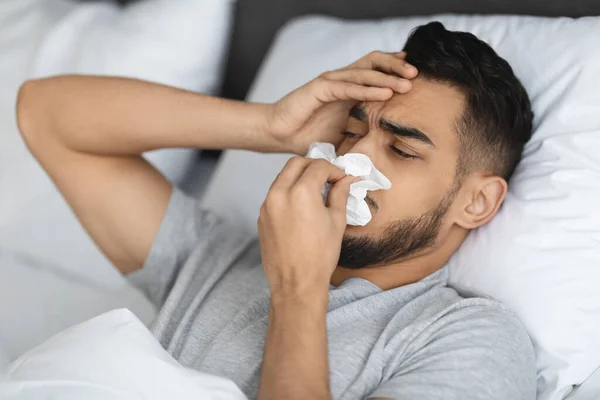 Seasonal Flu. Sick Arab Man Blowing Runny Nose While Lying In Bed — Stock Photo, Image