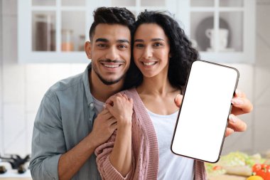 Happy middle eastern couple holding smartphone with empty screen