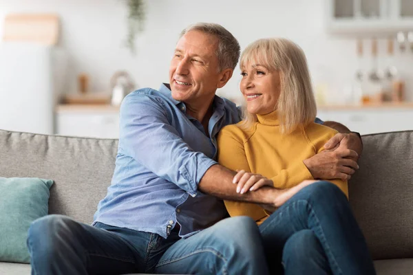 Happy Mature Spouses Hugging Looking Aside Sitting On Couch Indoor — стокове фото