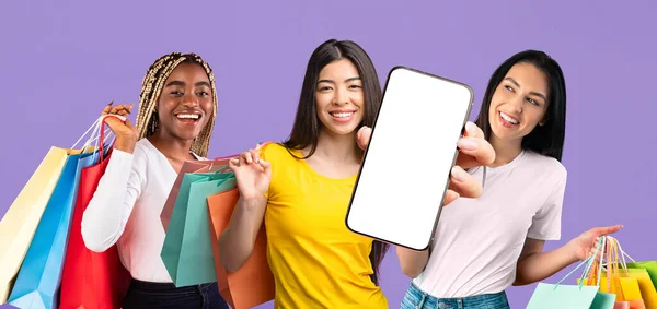 Three multiracial girlfriends shopaholics showing smartphone with blank screen — Stockfoto