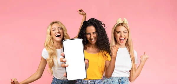 Carefree millennial ladies having fun, showing smartphone, mockup — стоковое фото