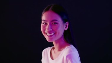 Half-Turned Asian Female Laughing At Camera While Standing Illuminated By Neon Light