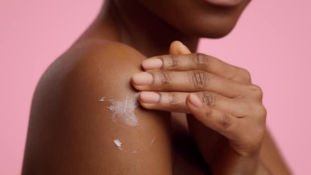 Unrecognizable Black Woman Applying Cream Moisturizer On Shoulders, Pink Background — Vídeo de Stock