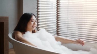Attractive Young Asian Female Relaxing In Bathtub Filled With Foam