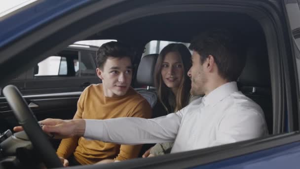Πωλήσεις αυτοκινήτων. Νεαρό ζευγάρι που επιλέγουν νέο όχημα μιλάμε με αντιπρόσωπο κάθεται στο αυτοκίνητο στο κατάστημα αντιπροσωπείας, μεγέθυνση σε πλάνο — Αρχείο Βίντεο