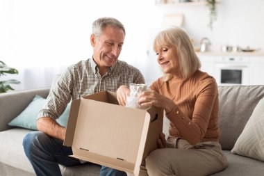 Older Couple Unpacking Box With Vase After Shopping At Home