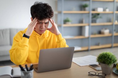 Stressed Asian male sitting at desk with pc