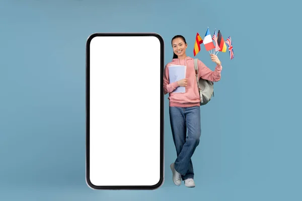 快乐的亚洲女人，背着背包，拿着旗子站在手机旁边 — 图库照片