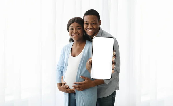 Expecting couple showing phone with empty screen, mockup — Stock Photo, Image