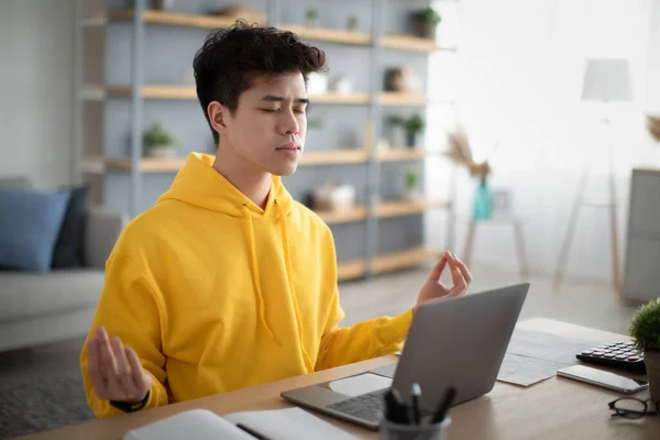 Asian man meditating with closed eyes in front of laptop — стокове фото