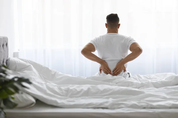Uncomfortable Bed. Young Man Waking Up With Lower Back Pain, Rear View — Stock fotografie