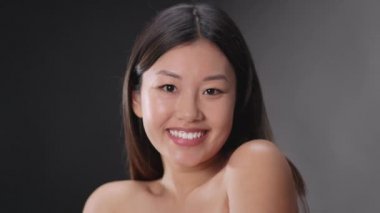 Flirty happy asian lady model with bare shoulders dancing and fooling around, smiling to camera, slow motion
