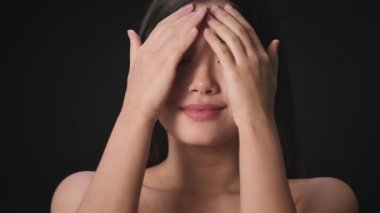 Face care procedures. Young beautiful asian lady caressing her face, enjoying her smooth skin, black background
