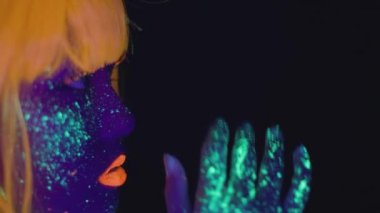 Graceful asian lady with bright neon body art wearing orange wig dancing over black studio background, empty space