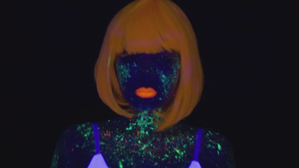 Young asian woman wearing orange wig with fluorescent makeup coming to camera and dancing over black background — Stockvideo