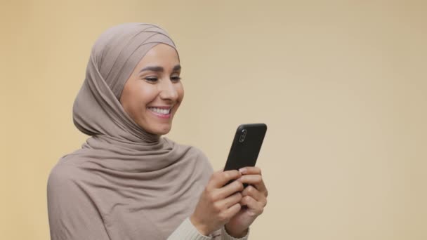 Comunicación en línea. Joven dama positiva de Oriente Medio en mensajes de texto hijab o navegar por la web en el teléfono inteligente, espacio libre — Vídeos de Stock