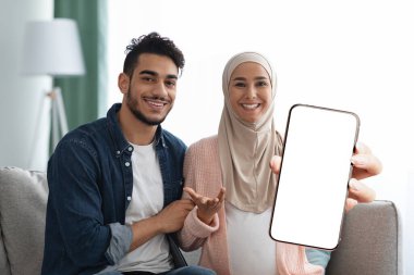 Happily married pregnant muslim couple showing smartphone, mockup