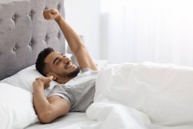 Lazy Morning. Pleased Middle Eastern Man Stretching In Bed After Nice Sleep