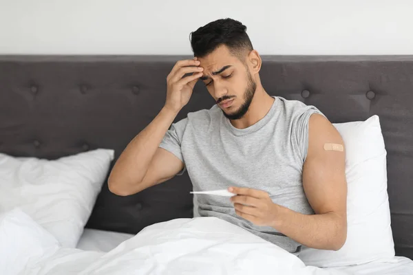 Vaccination Side Effects. Vaccinated Arab Guy With Plaster On Arm Holding Thermometer — Stock Fotó