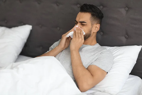 Sick Middle Eastern Man Blowing Nose In Paper Tissue In Bed — 图库照片