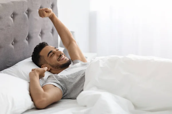 Τεμπέλικο πρωινό. Ευχαριστημένος μεσανατολίτης άντρας ξαπλωμένος στο κρεβάτι μετά τον ωραίο ύπνο — Φωτογραφία Αρχείου