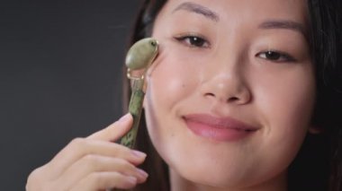 Skin lifting lifehacks. Portrait of young beautiful asian woman making self face massage with natural quartz massager