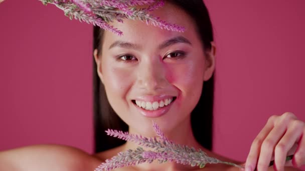 미녀 개념. 얼굴 가까이에 보라색 꽃을 피우는 젊은 아시아 여자를 가르치는 모습 — 비디오