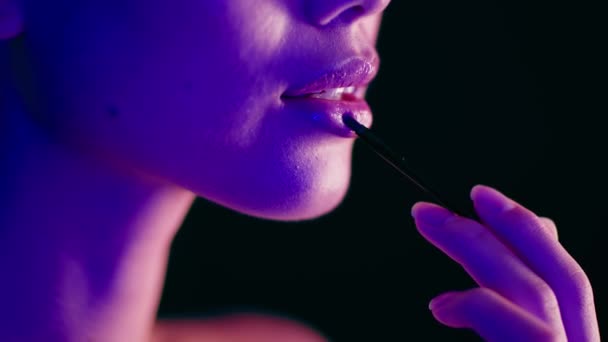 Нерозпізнана жінка освітлена фіолетовим неоновим світлом нанесення помади пензлем для макіяжу — стокове відео
