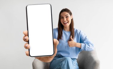 Phone Mockup. Cheerful Young Female Showing Big Smartphone With White Screen