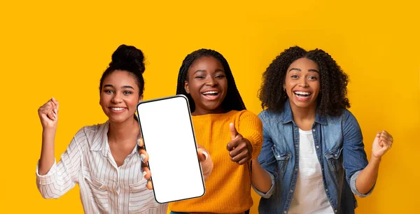 Three emotional black ladies gesturing on yellow, showing cellphone, mockup — Stock Fotó