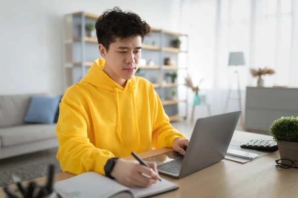 Skupiony azjata człowiek pracuje na laptopie i pisanie — Zdjęcie stockowe