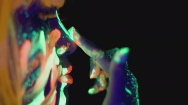 Side view portrait of woman with glowing neon makeup caressing face from lips to neck, glowing in uv lights, empty space