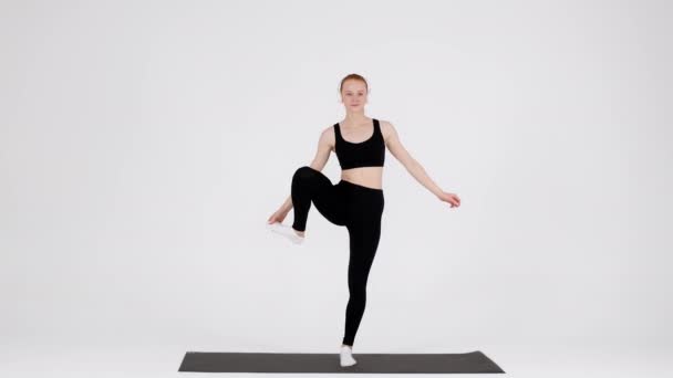 Молодая гибкая женщина практикует йогу в студии, поднимая ноги в сторону — стоковое видео