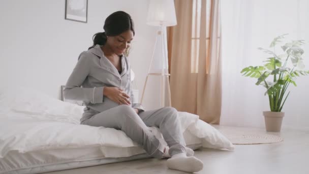 Peaceful young african american pregnant lady wearing pajamas resting on bed and caressing her big belly — Vídeo de Stock