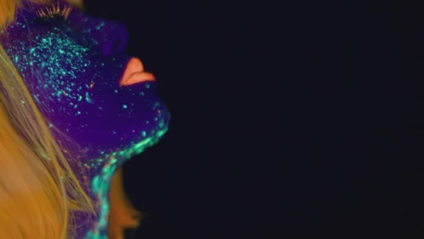 Jeune femme avec un maquillage au néon lumineux portant une perruque orange dansant sur fond de studio noir, espace vide — Video