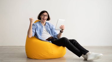 Online success. Satisfied guy with digital tablet celebrating win, raising fist and exclaiming with excitement, panorama