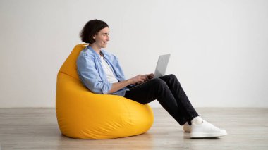 Freelance career. Young man working with laptop computer, sitting in beanbag chair, enjoying remote work opportunities
