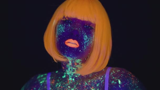 Студійний портрет молодої азіатки з ультрафіолетовим мистецтвом тіла і макіяжем і носінням помаранчевої перуки, що позує на чорному тлі — стокове відео