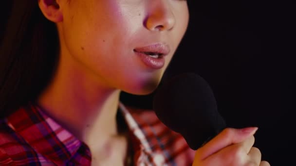 Крупним планом Портрет молодої азіатки співає в мікрофон над темним тлом — стокове відео