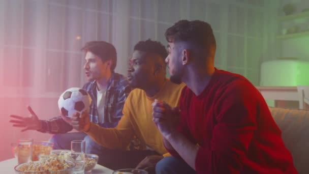Emocional diversos hombres jóvenes viendo la televisión con el deporte por la noche y beber cerveza, el apoyo de equipo favorito con pelota de fútbol — Vídeo de stock
