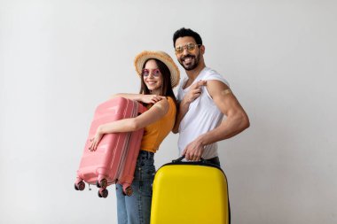 Ready for travel. Young vaccinated couple showing shoulders with band aid after Covid-19 vaccine, holding suitcases