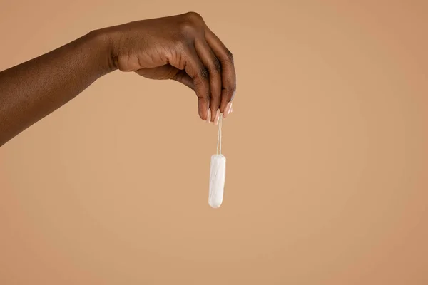 Hand of black woman holding tampon over beige studio background — Foto Stock