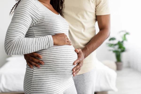 Cropped millennial african american man hugs belly of pregnant lady in bedroom interior, empty space — Fotografia de Stock