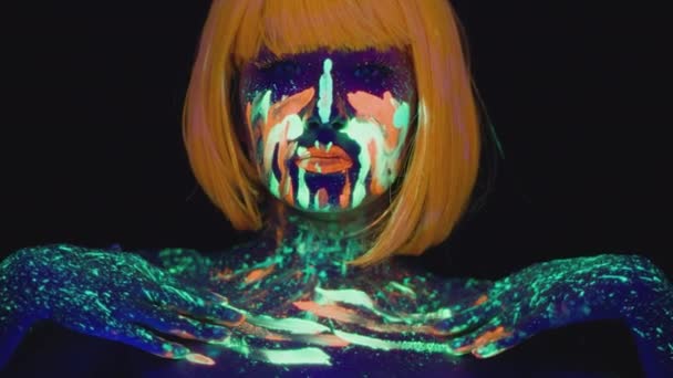 Mode porträtt av ung kvinna med ljusa ultraviolett neon kropp konst bär orange peruk dans till kameran — Stockvideo