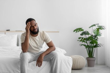 Desperate young african american guy with beard suffers from loneliness, depression in bedroom interior