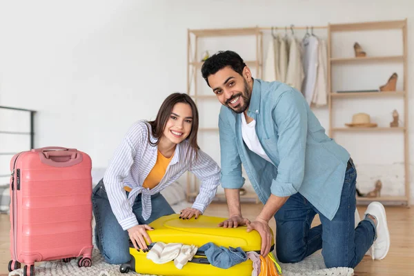 Preparación de viaje. Feliz pareja multirracial empacando y tratando de cerrar la maleta, preparándose para las vacaciones en casa — Foto de Stock